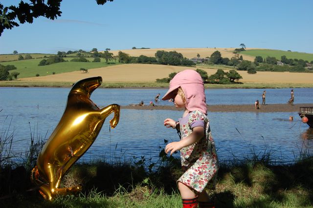 child with golden horse balloon beside a river